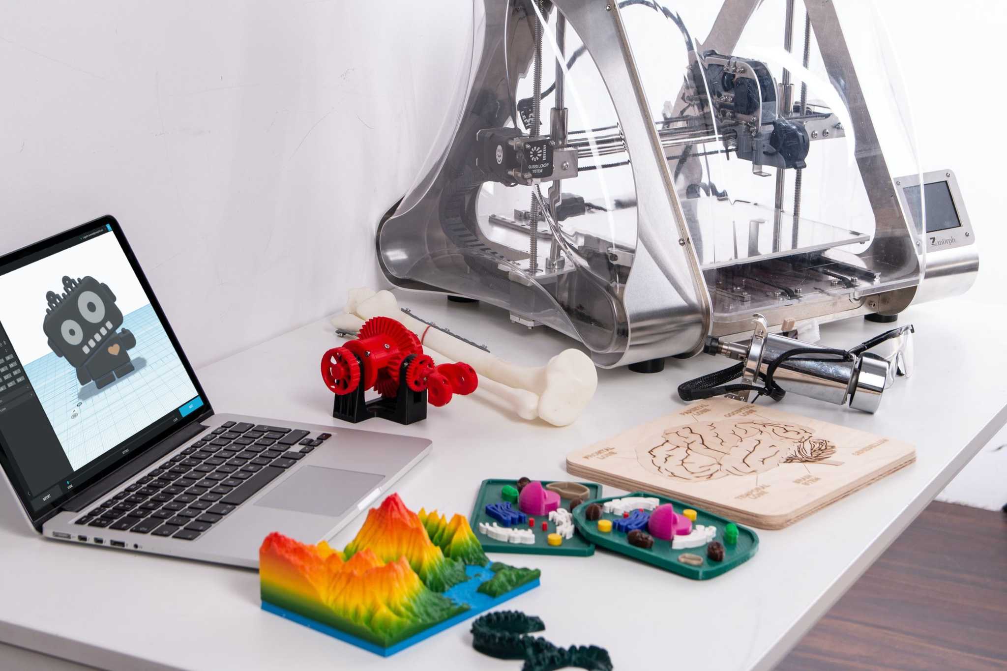 Laptop, 3d printer and a number of 3d printed colourful models on a desk